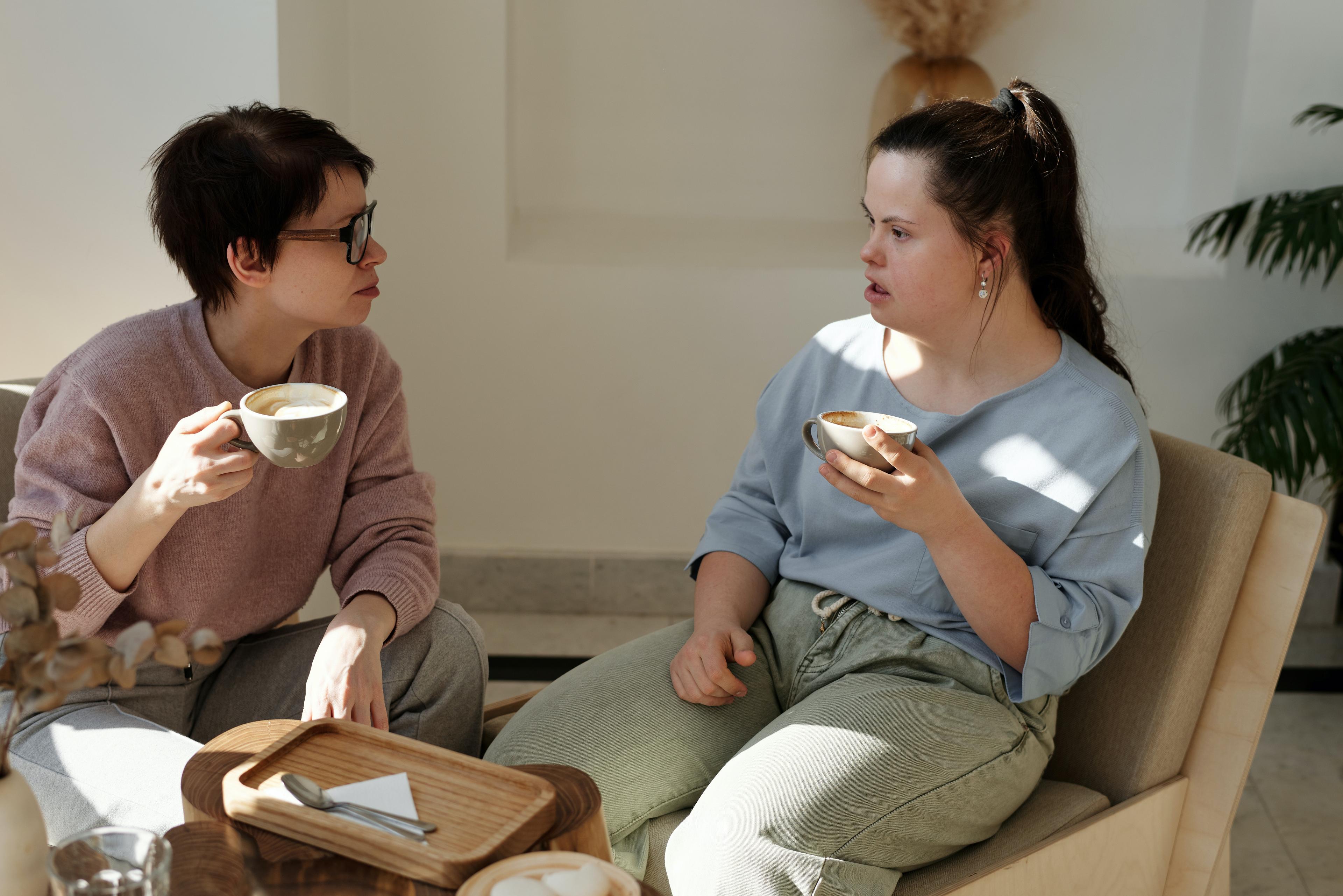 Zwei Personen sitzen sich gegenüber und scheinen in ein gespräch vertieft zu sein. Beide halten jeweils eine Tasse in der Hand.